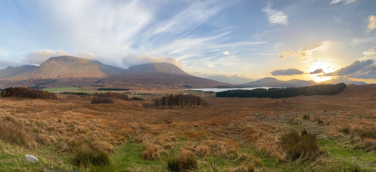 Panoramic view of Glencoe at sunset, with golden light casting over the dramatic Highland landscape.