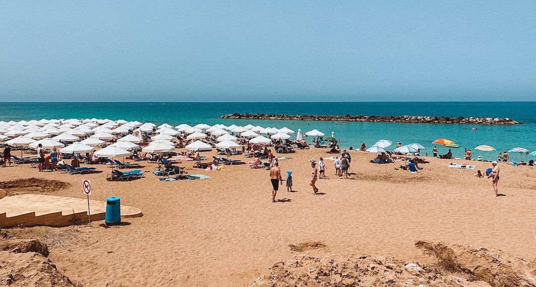 A typical beach in Paphos with sunbeds, parasols, and clear blue Mediterranean water, capturing the summer vibe